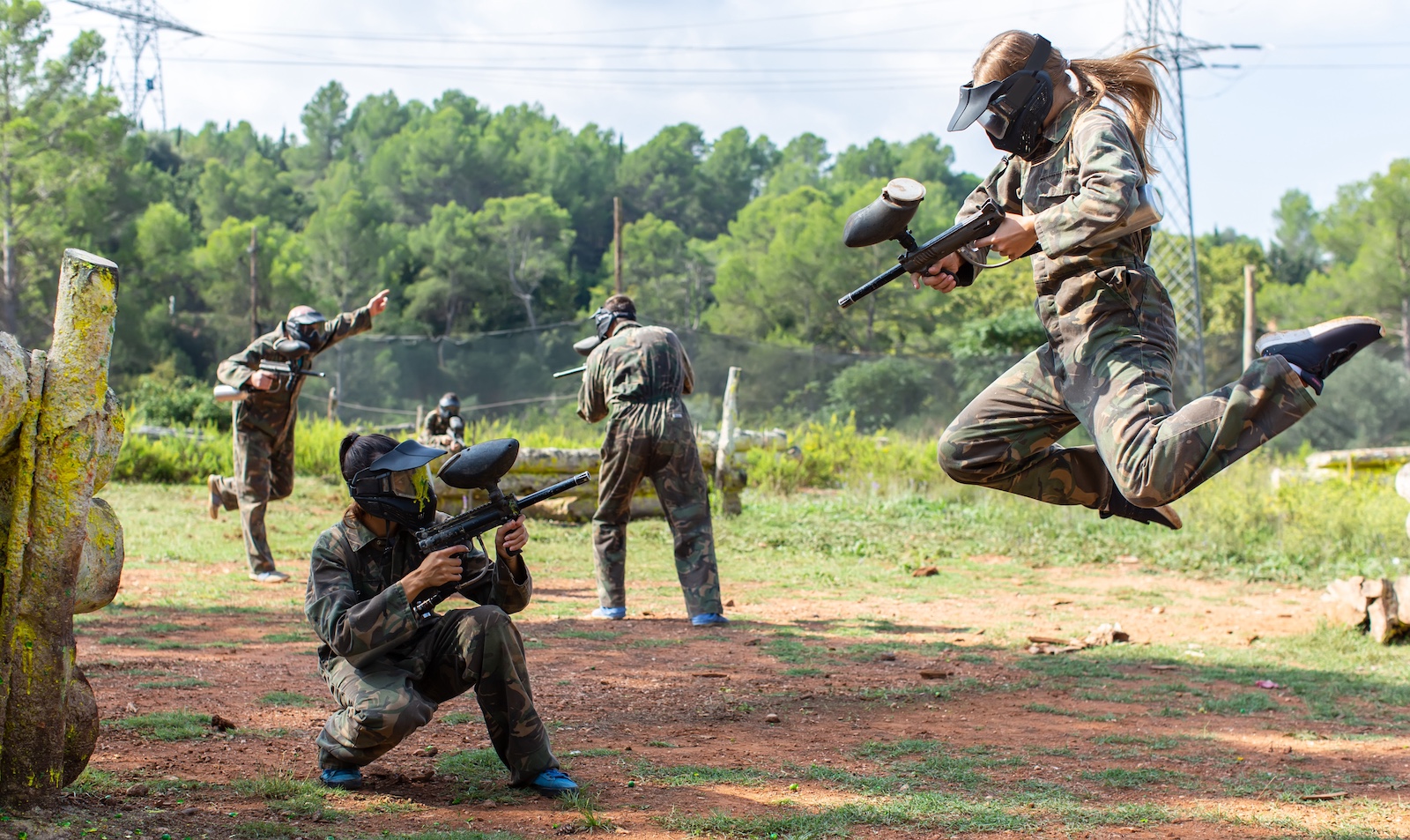 Dynamic paintball battle. Portrait female player jumping and aiming marker on member of opposing team